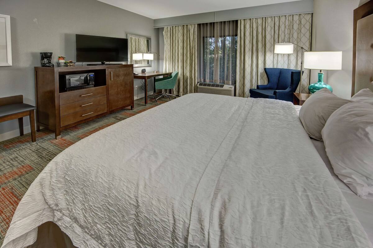 A hotel room with a large bed, a desk with a chair, a television, a coffee maker, and a window with curtains.