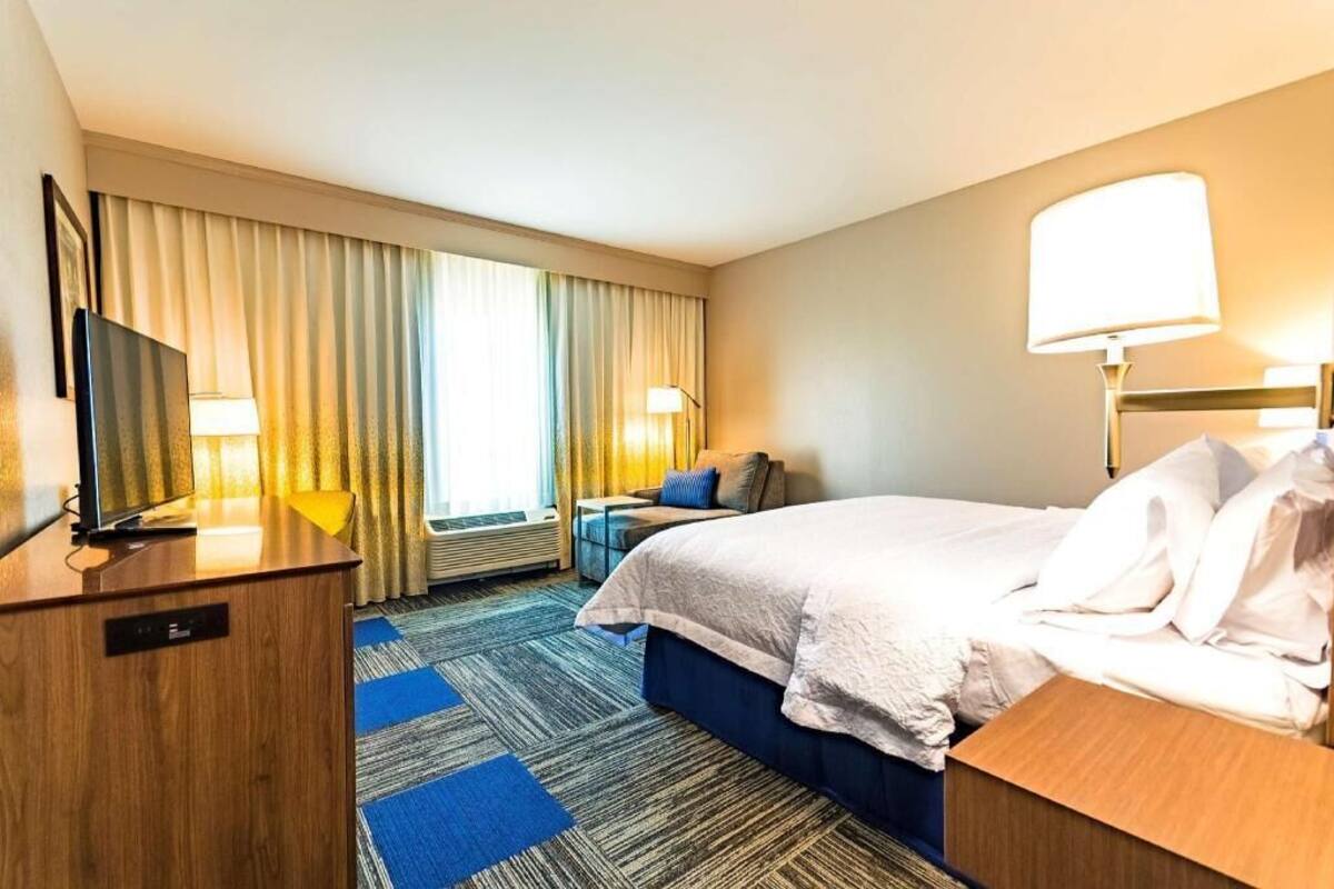 A hotel room with a bed, a desk, a television, and a window with curtains.