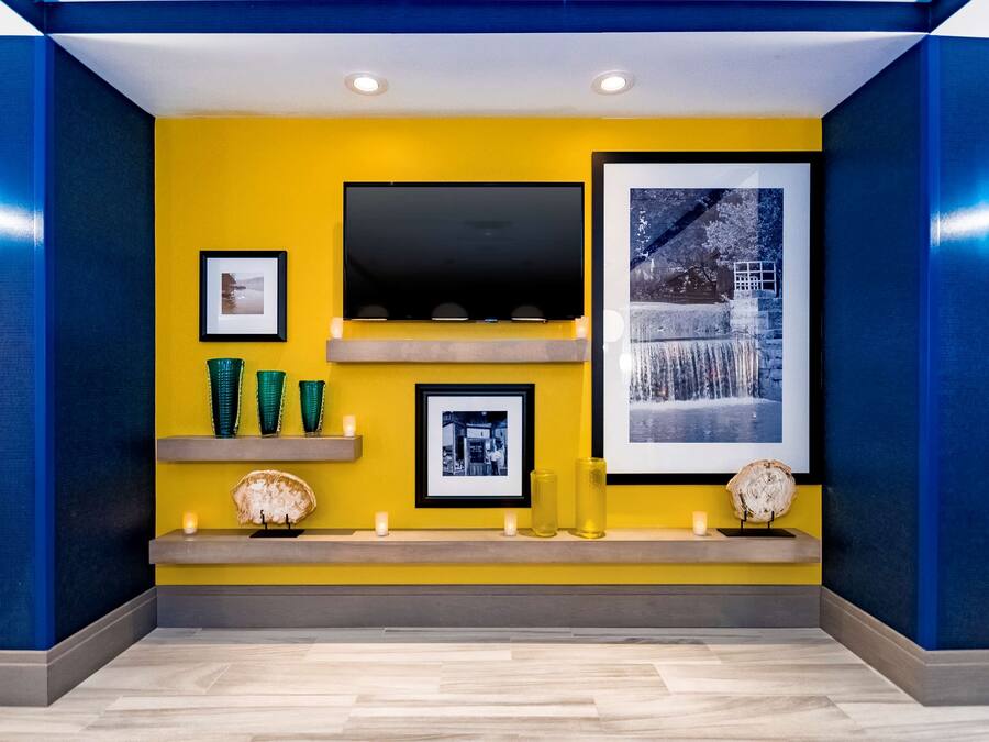 Una sala de estar moderna con una pared de acento amarilla, un televisor de pantalla plana, cuadros enmarcados y objetos decorativos en estantes.