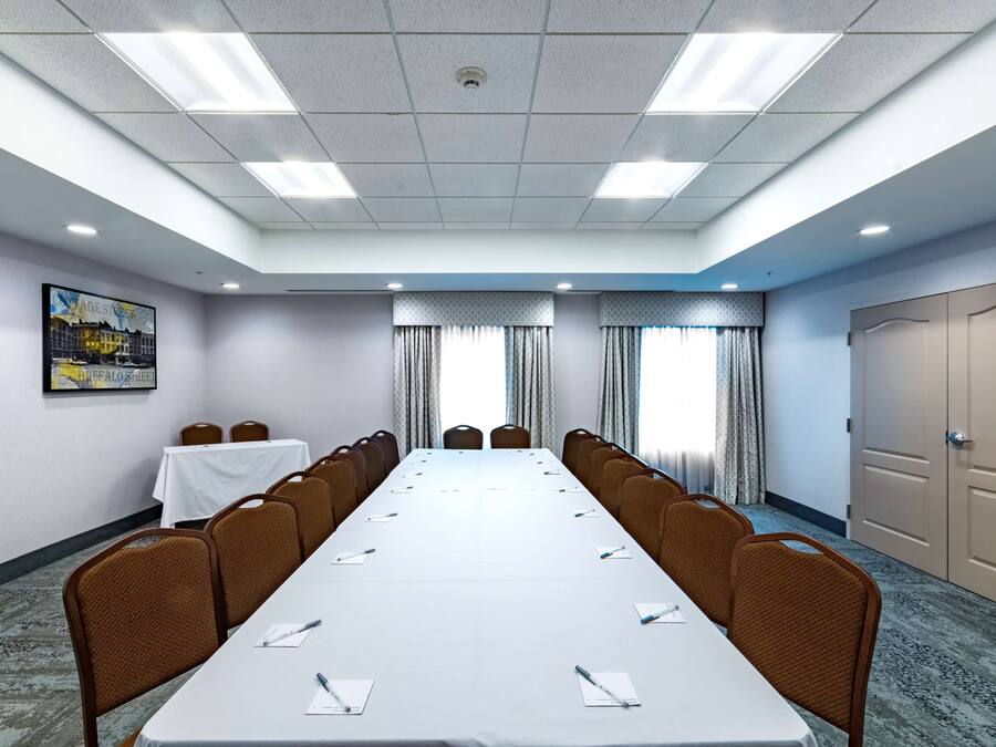 Ett konferensrum med ett långt bord, stolar, en projektorduk och en dörr.