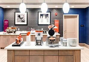 A modern kitchen area with a waffle maker, coffee machine, and various condiments.