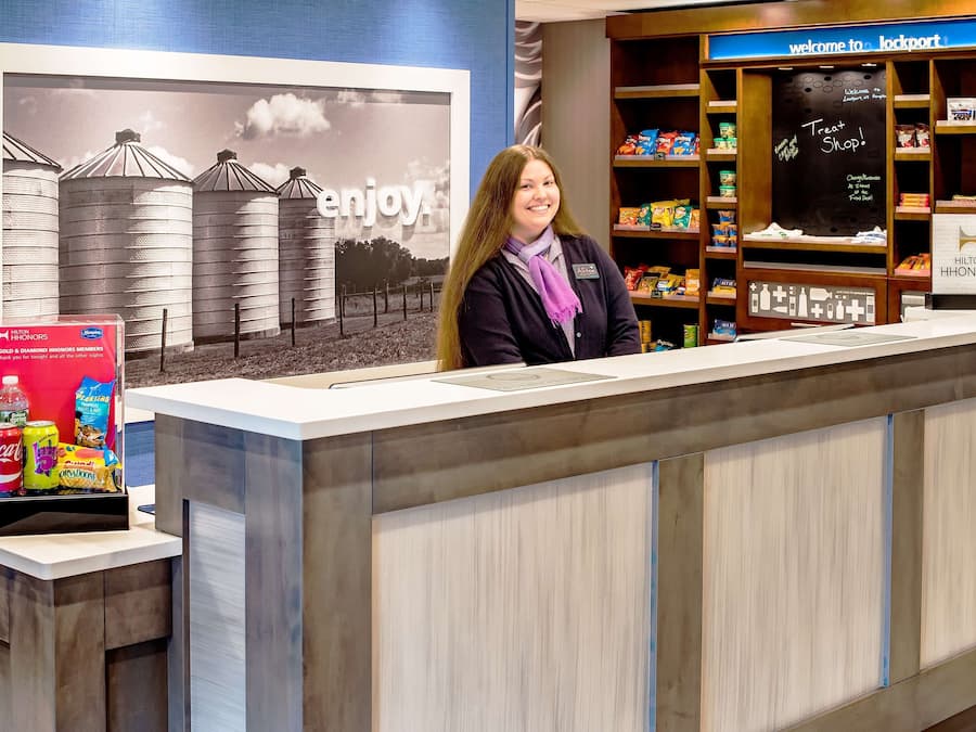 Una reception hotel con un’ampia foto incorniciata di silos, un cartello con la scritta “Goditi” e un cartello che indica “Pasticceria”.