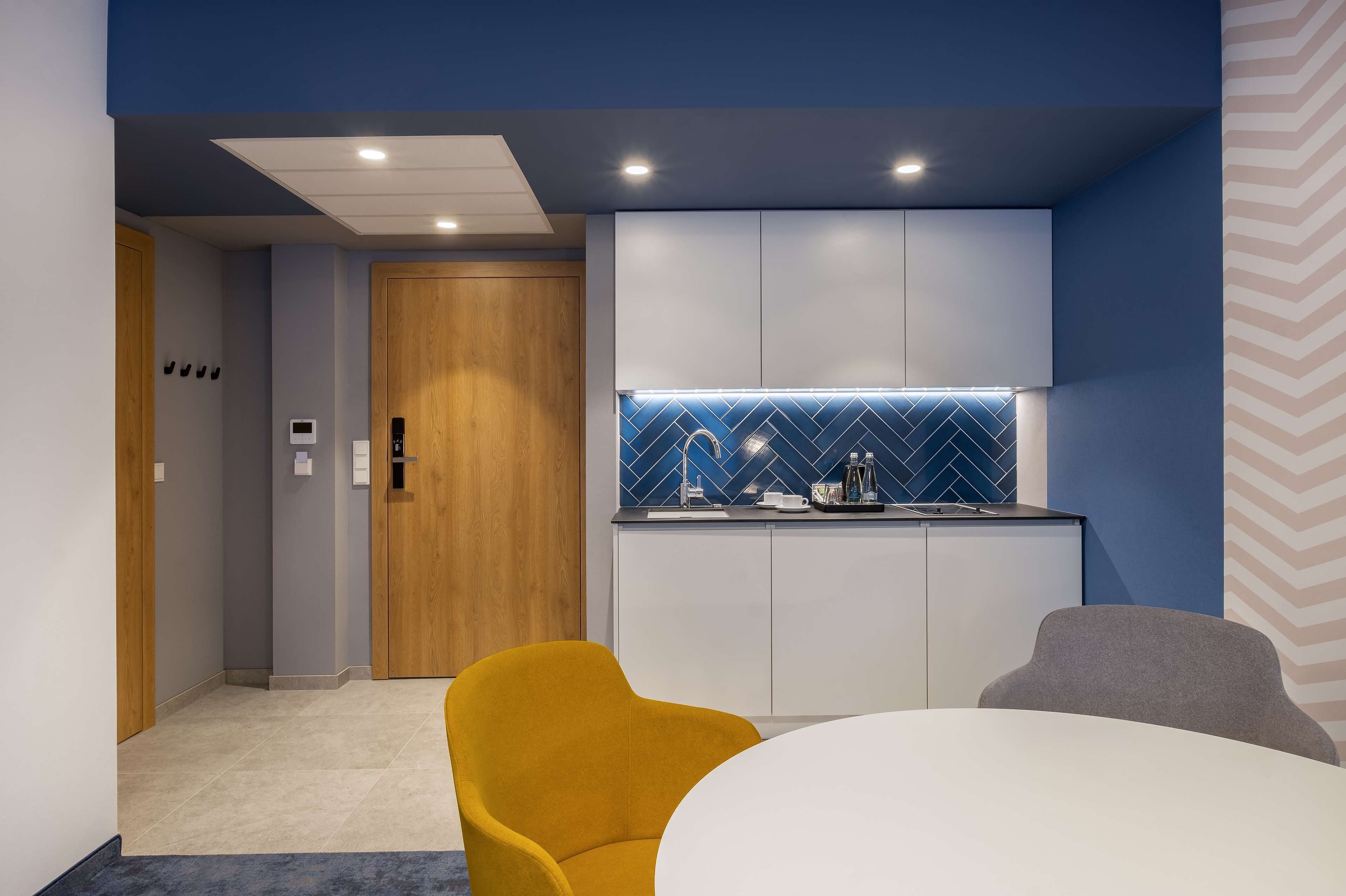 A modern kitchen with a blue backsplash, white cabinets, and a wooden door.