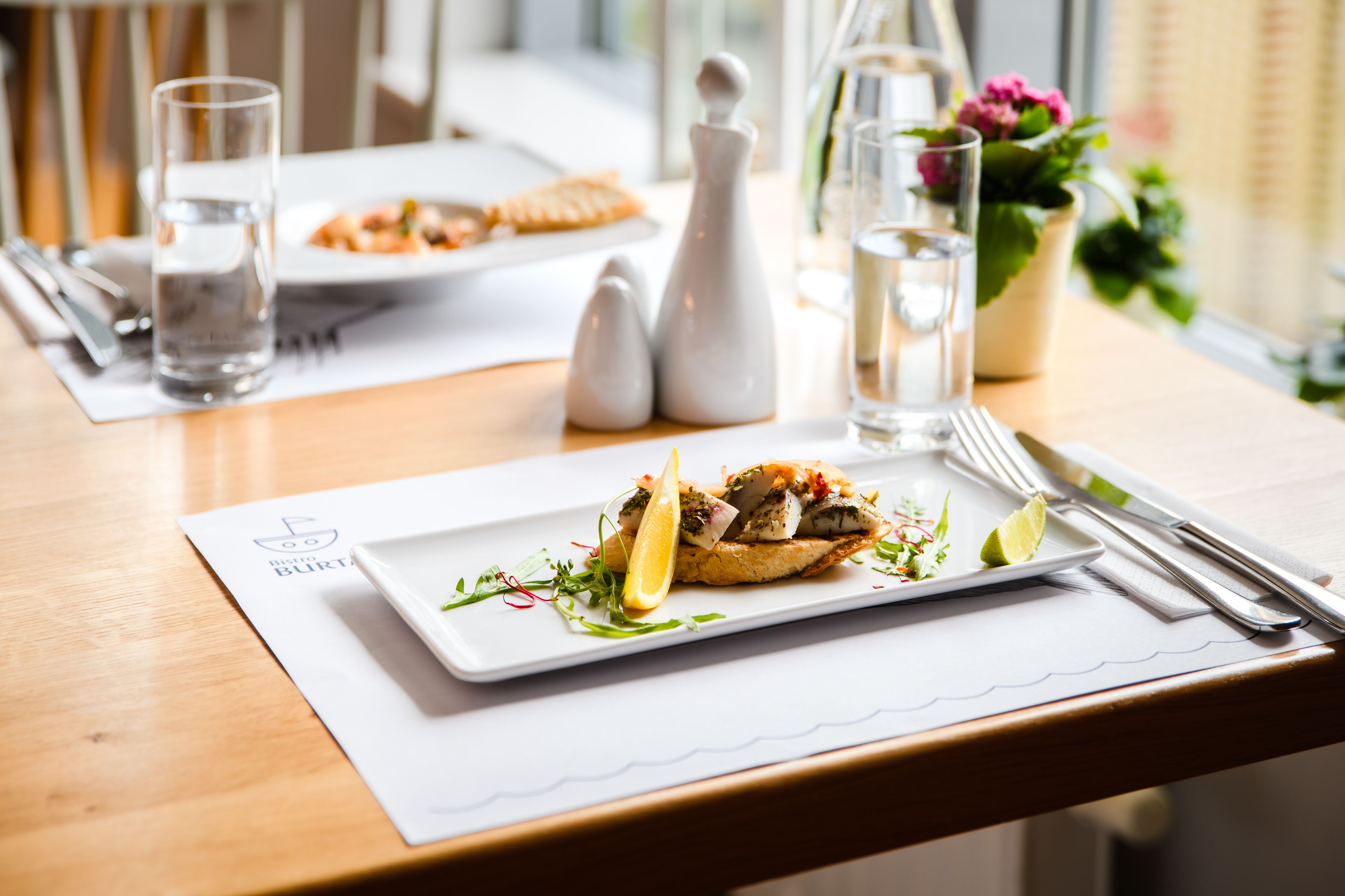 Una mesa de comedor dispuesta con platos de comida, cubiertos y vasos de agua.