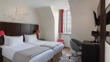 Quarto de hotel com duas camas, uma escrivaninha com cadeira, televisão e janela com cortinas.