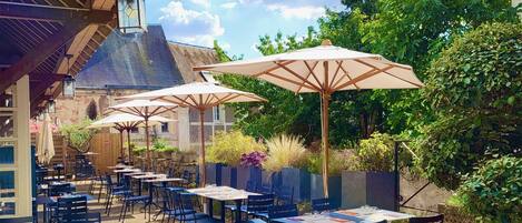 An outdoor café with tables and chairs, umbrellas, and a view of the sky and trees.