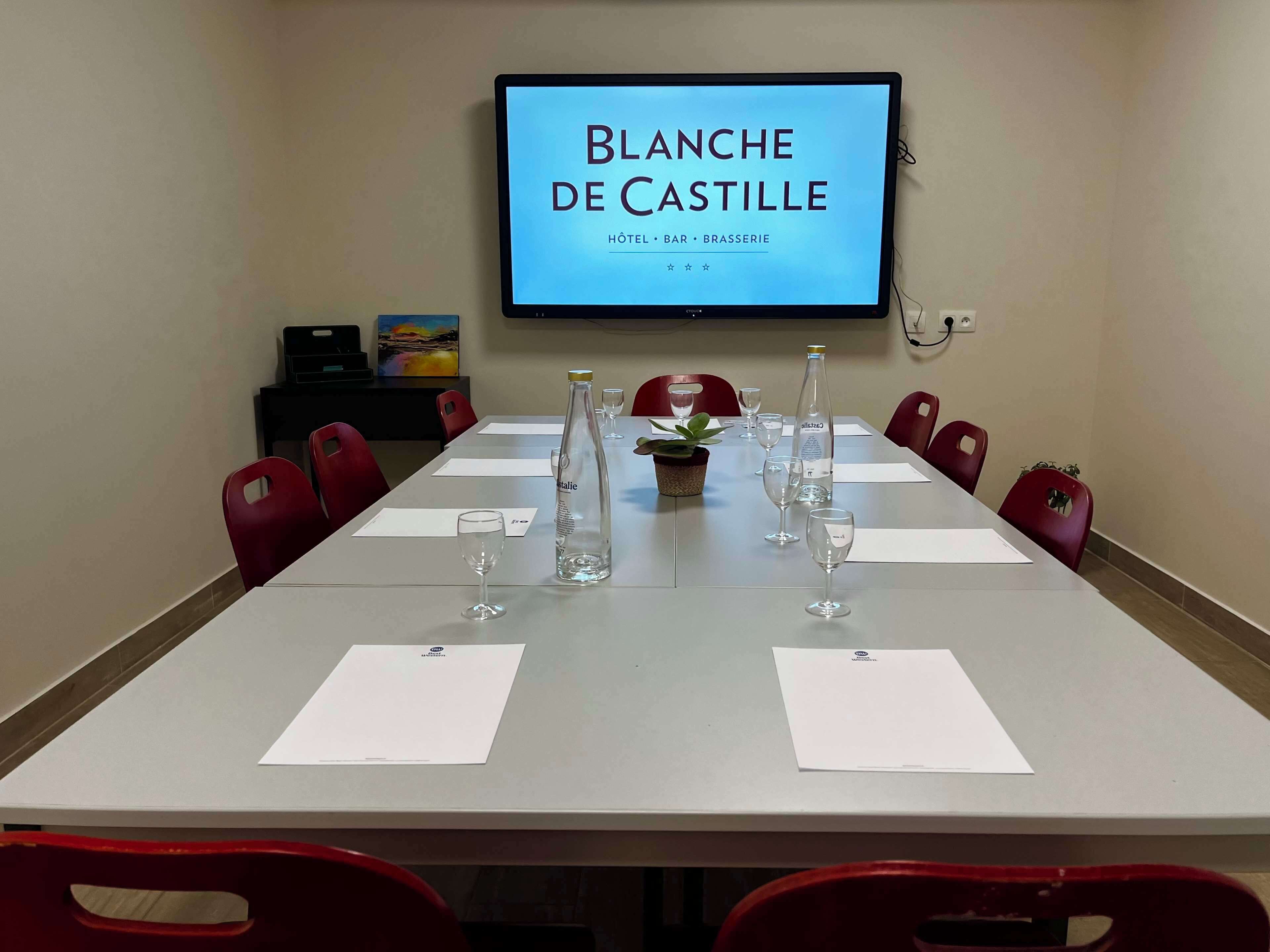A conference room with a long table, red chairs, and a television screen displaying "BLANCHE DE CASTILLE HOTEL BAR BRASSERIE".