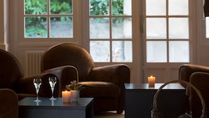 A cozy seating area with leather chairs, a small table with two glasses and a candle, and a view through large windows.