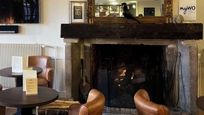 A cozy room with a fireplace, leather chairs, a table with menus, and a large mirror above the fire.