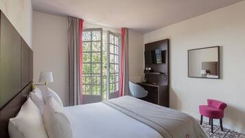 A hotel room with a bed, a desk, a chair, a TV, and a window with curtains.