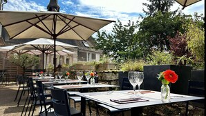 An outdoor dining area with tables and chairs, large umbrellas, and a stone wall.