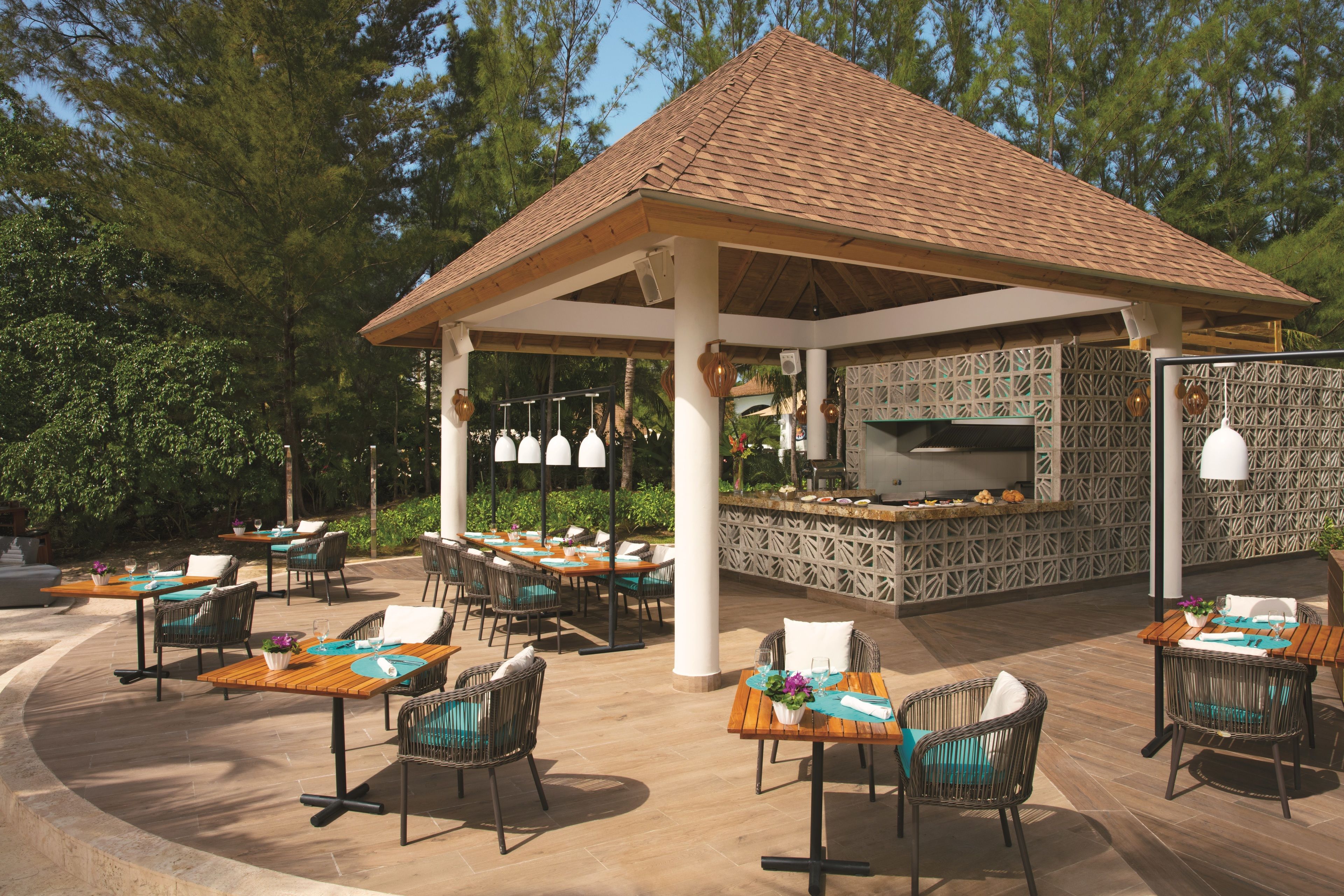 Una terrazza esterna con diversi tavoli e sedie, un'area salotto coperta e un barbecue integrato.