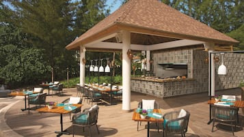 Una terrazza esterna con diversi tavoli e sedie, un'area salotto coperta e un barbecue integrato.