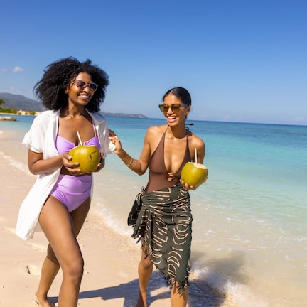 Two people walking on a beach holding coconuts.