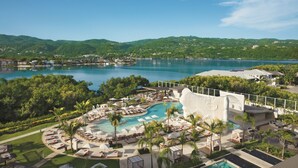 Un resort con una gran piscina, zonas de descanso y vistas a las colinas y al agua circundantes.