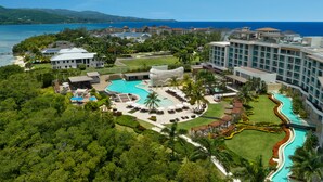 Un resort con una gran piscina, varias edificaciones para huéspedes y vista al océano.