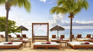 Un resort en la playa con sillones de madera, una cama con dosel y palmeras.
