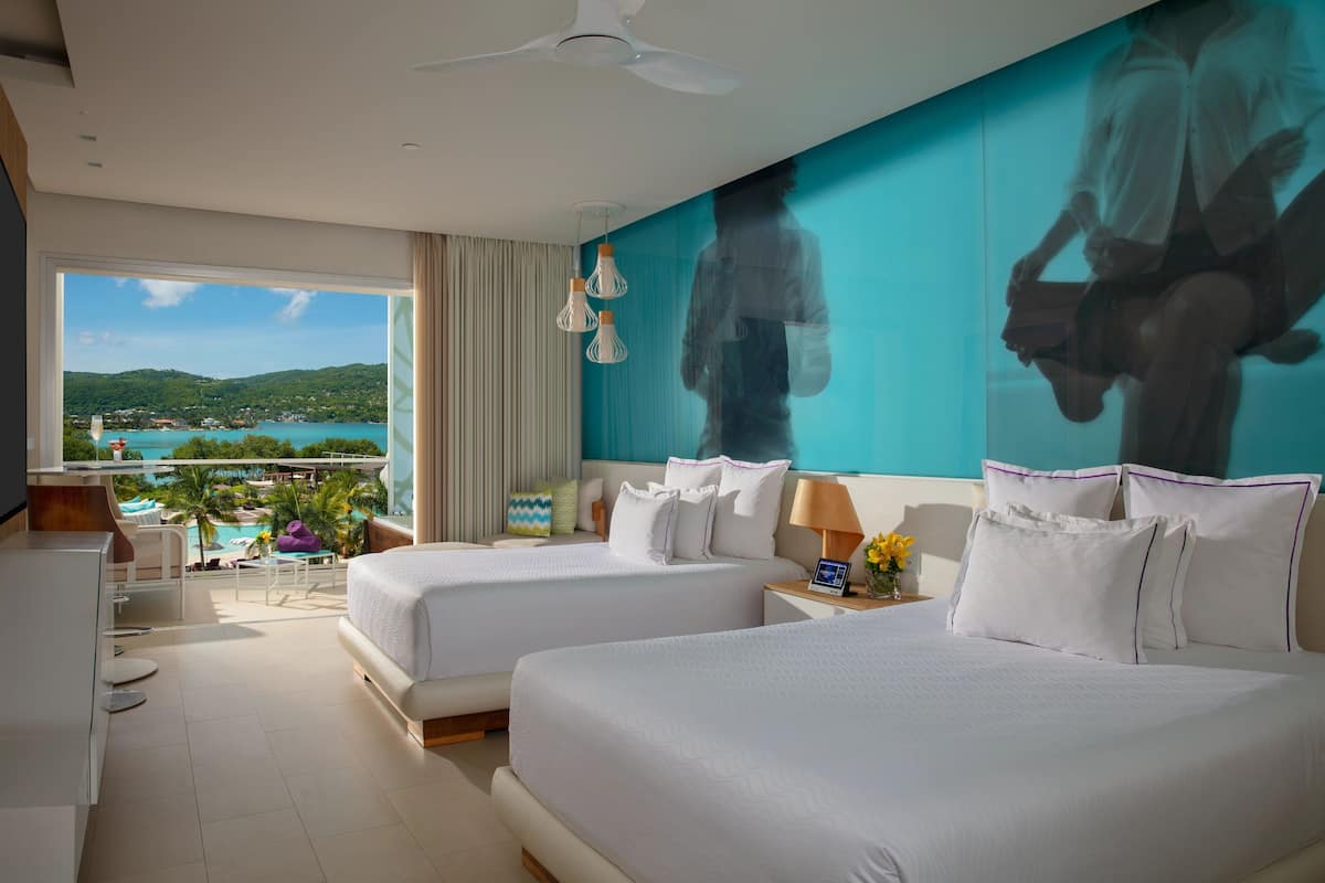 Een hotelkamer met twee bedden, een balkon en uitzicht op een waterlichaam.