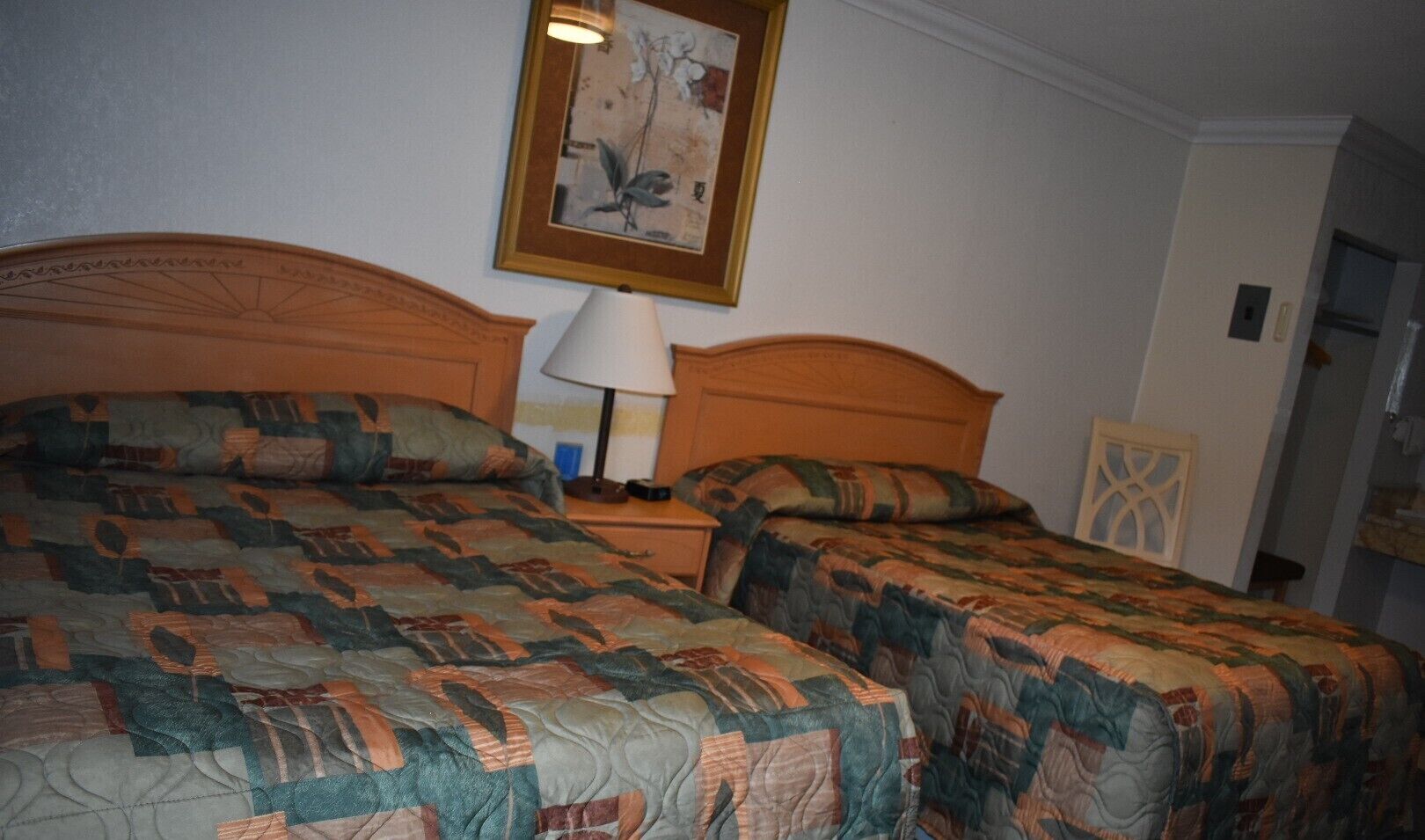 Habitación doble con dos camas, cada una con una colcha estampada, una mesita de noche con lámpara y una obra de arte enmarcada en la pared.