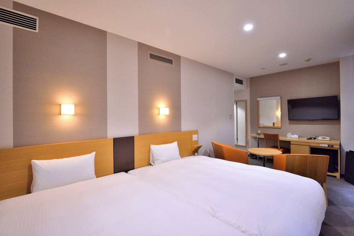 Quarto de hotel com uma cama grande, duas mesas de cabeceira, uma escrivaninha com cadeira, televisão de tela plana e luminárias fixadas na parede.