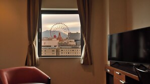 Quarto de hotel com uma janela grande, uma televisão, uma cadeira vermelha e uma mesa pequena.