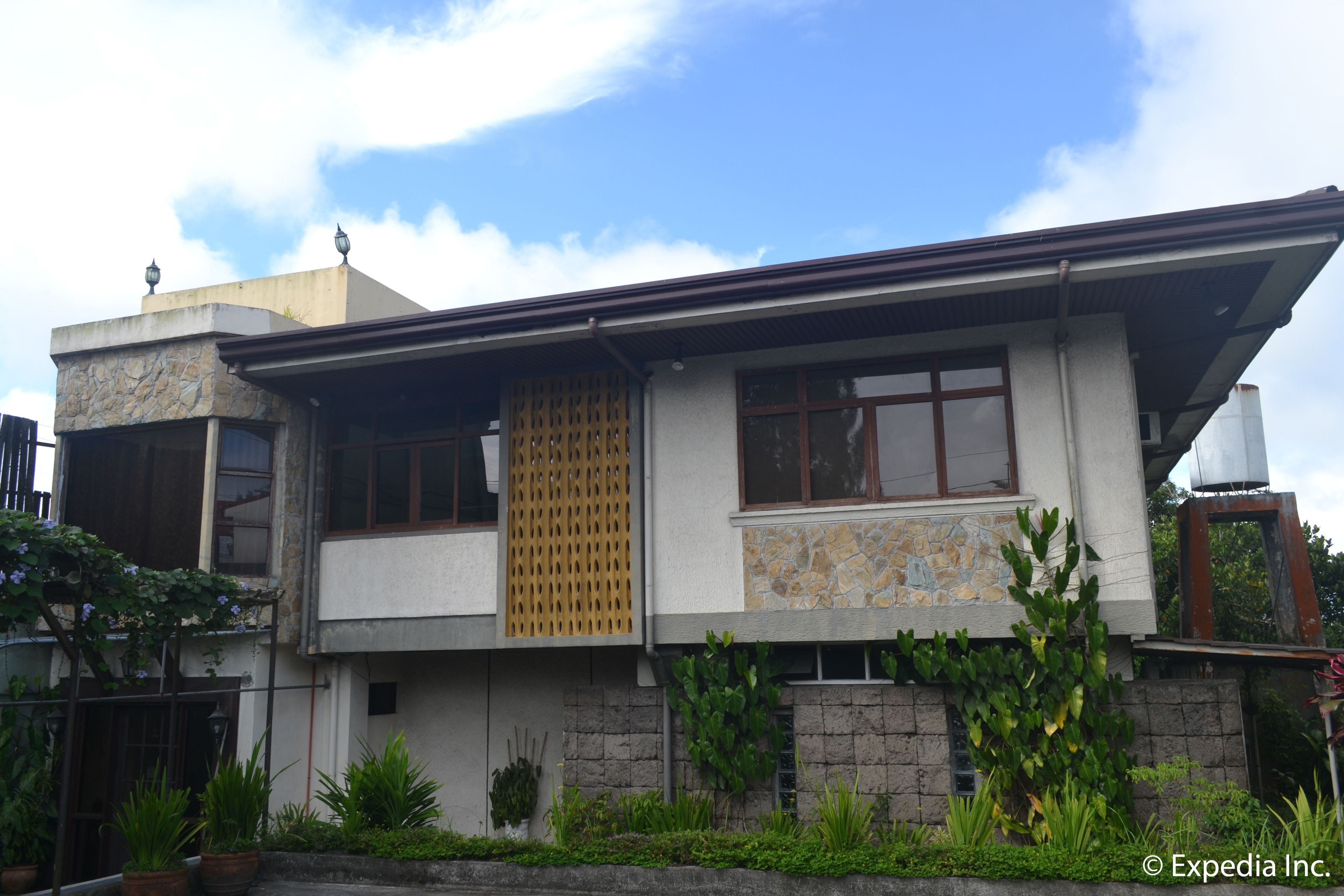 A two-story house with a stone facade, a wooden lattice window, and a metal roof.