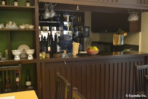 Una zona de bar con estantes llenos de botellas, un frutero y una pantalla de televisión.