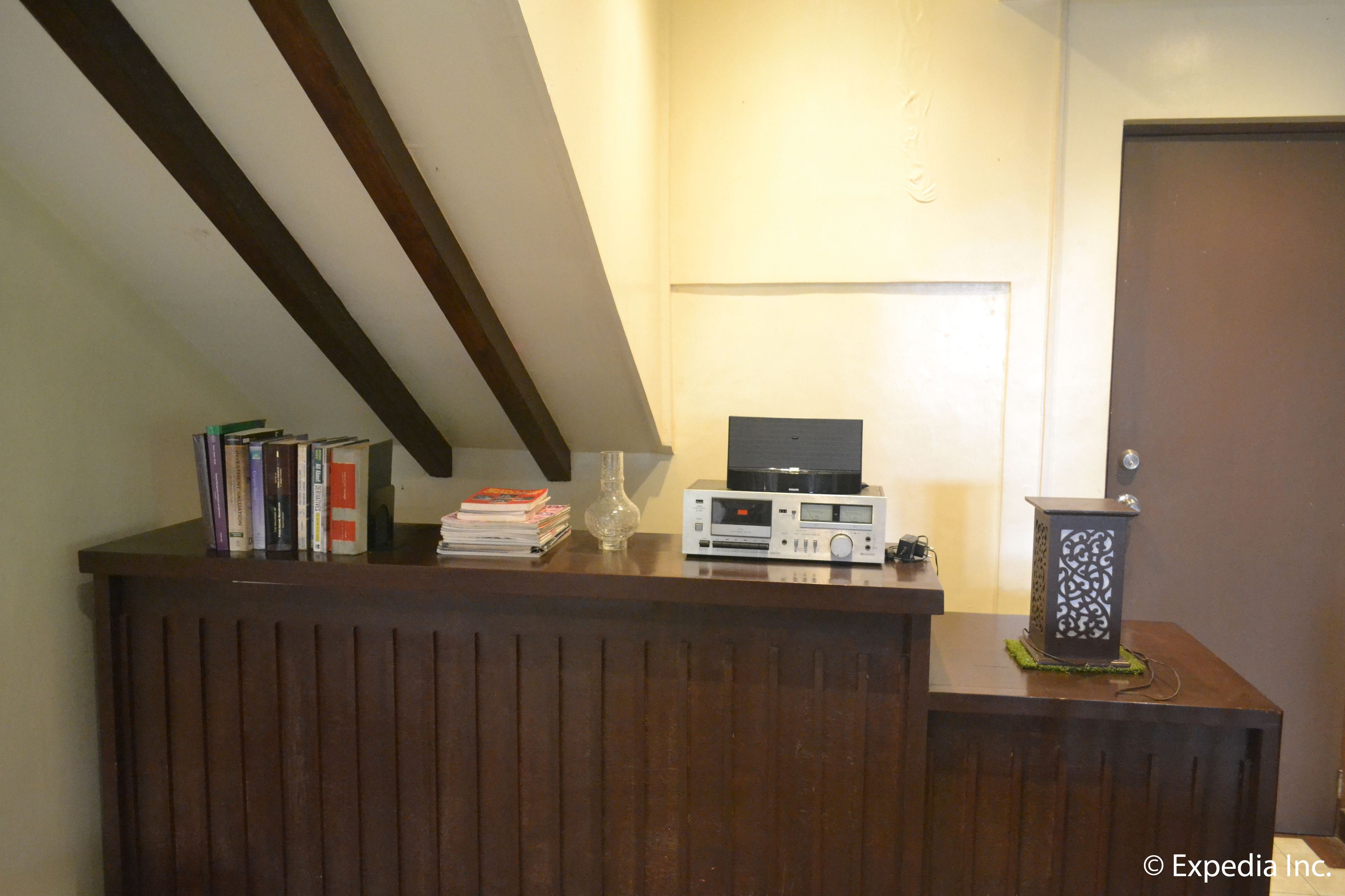Uma mesa de recepção com um rádio, livros, um vaso decorativo e uma porta ao fundo.