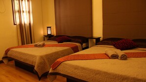 Two adjacent beds with neatly folded towels, a nightstand with a lamp, and a window with curtains. - Twin Pines Suites (Tagaytay)