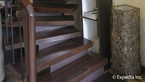 A wooden staircase with a handrail, a shelf with decorative items, and a patterned rug at the bottom. - Twin Pines Suites (Tagaytay)