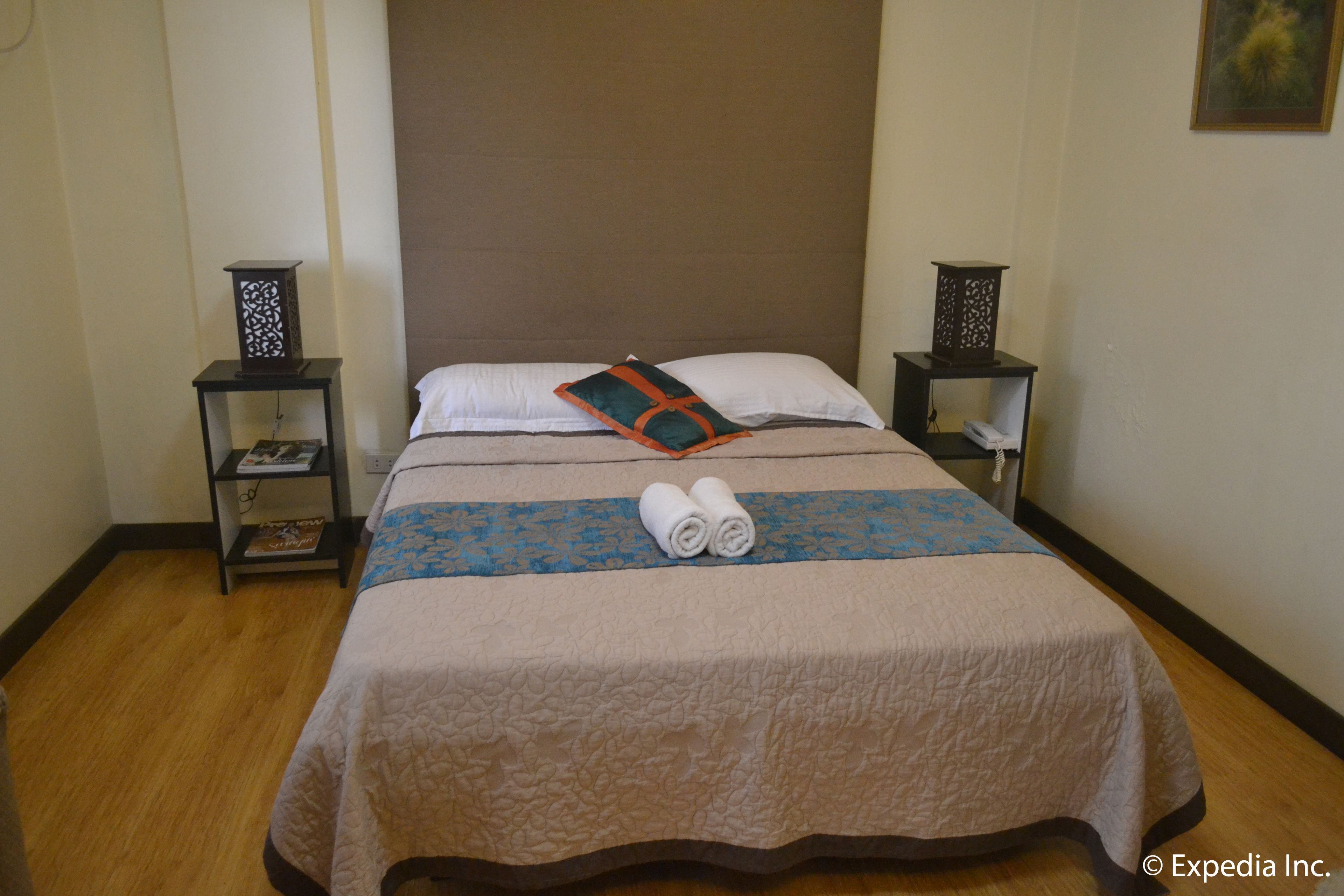 A neatly made bed with a quilt, two pillows, and rolled towels. There are two nightstands with decorative lamps and a book on one.