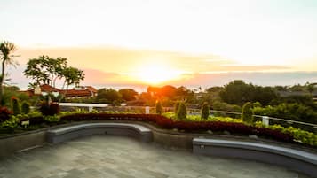 A courtyard with a curved pathway, surrounded by well-maintained greenery and a view of the sunset over a distant landscape.