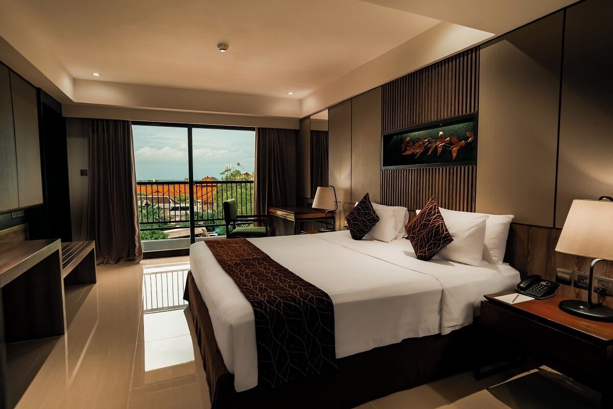 A modern hotel room with a large bed, a desk, a chair, and a balcony with a view.