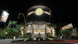 A modern building with a circular design, featuring a prominent illuminated logo at the center.