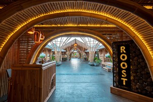 Une arche en bambou mène à un espace d’accueil où est affiché un panneau indiquant « ROOST ».