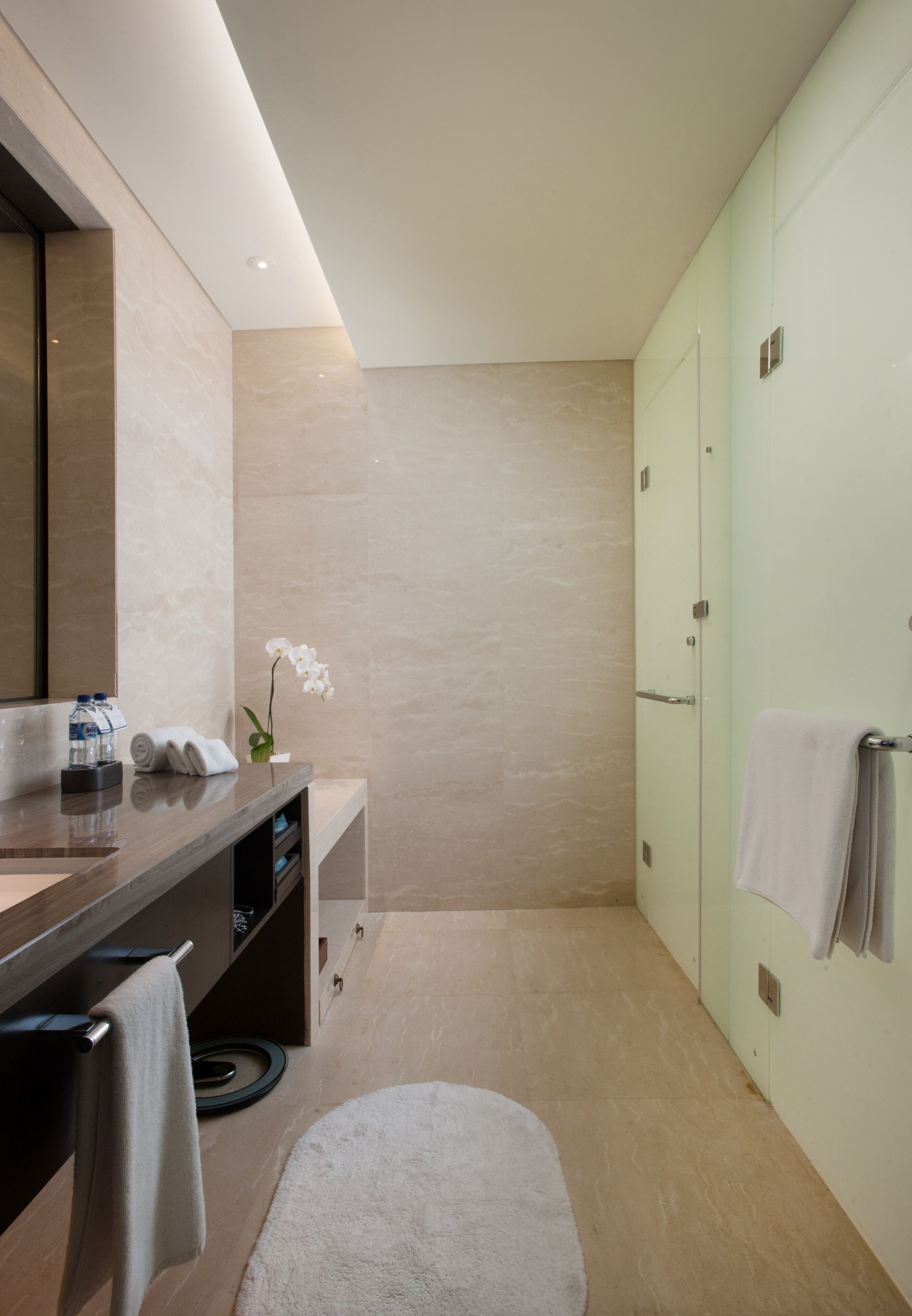 A modern bathroom with a large mirror, a towel rack, a sink with toiletries, and a small orchid plant.