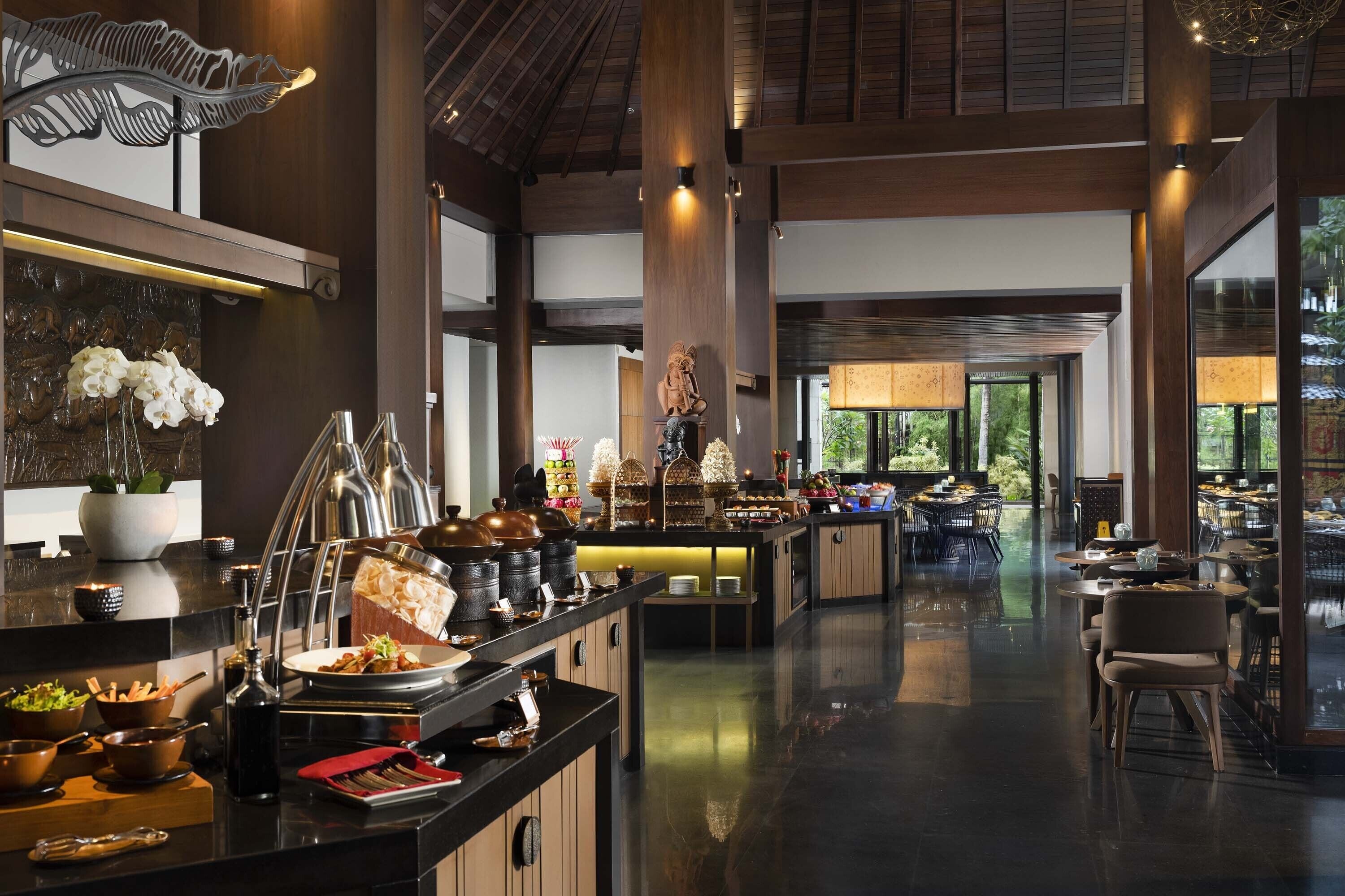 A spacious hotel lobby with a buffet area, wooden beams, and a view of greenery outside.
