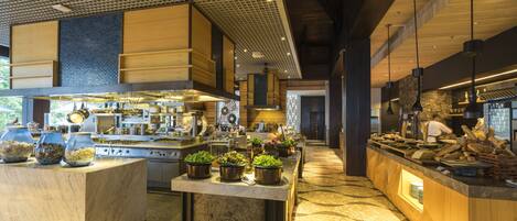 A modern kitchen with a central island, various cooking stations, and a long counter with food displays.