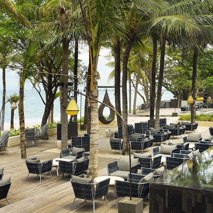 A beachside lounge with outdoor seating and a pool, surrounded by palm trees and overlooking the sea.