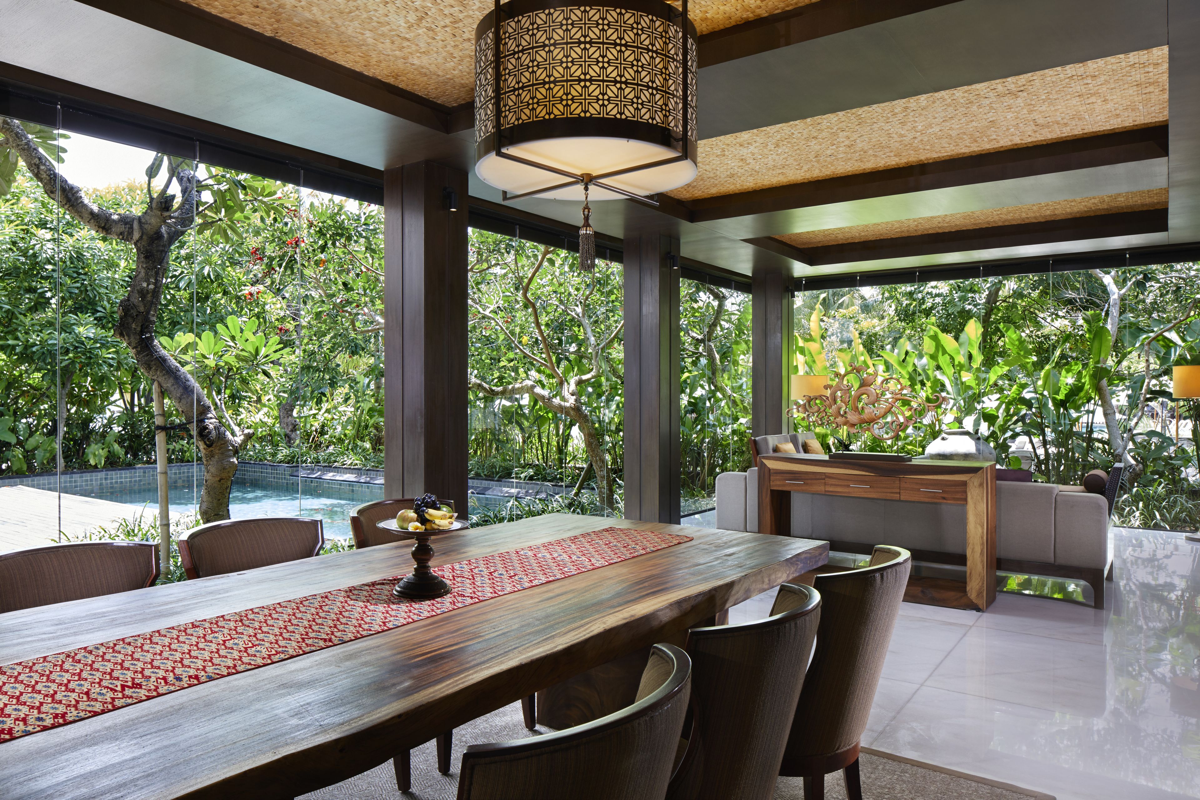 A dining area with a wooden table, chairs, and a red patterned runner. There is a hanging light fixture above the table.