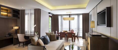 Una habitación de hotel moderna con sofá, mesa de comedor, sillas, televisor y escritorio con lámpara.