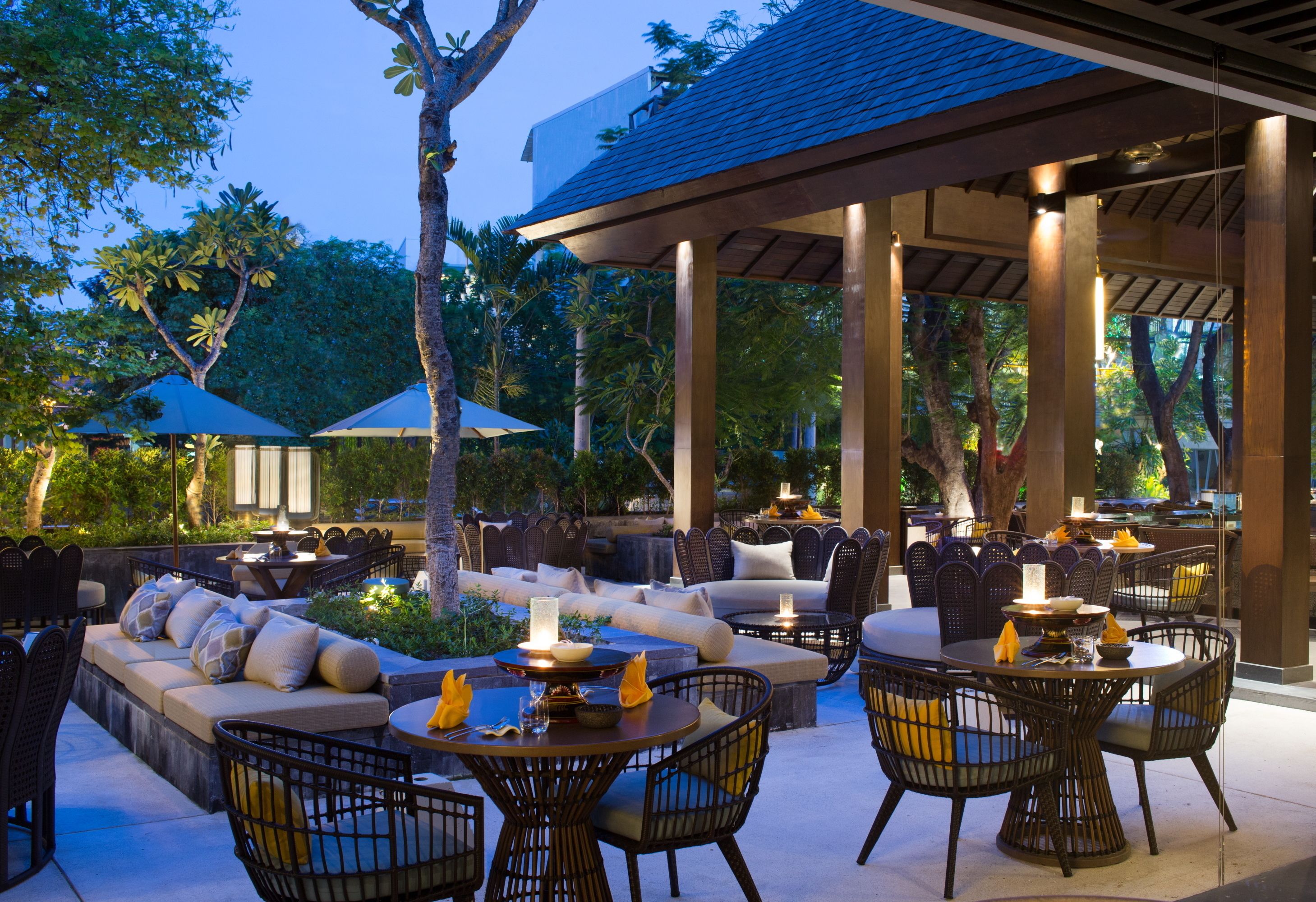 Un espace extérieur aménagé en terrasse, avec des coins salon comprenant des canapés et des fauteuils, ainsi qu’une table à manger.