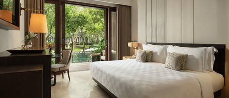 A hotel room with a large bed, a desk, a chair, and a view of a garden through the window.
