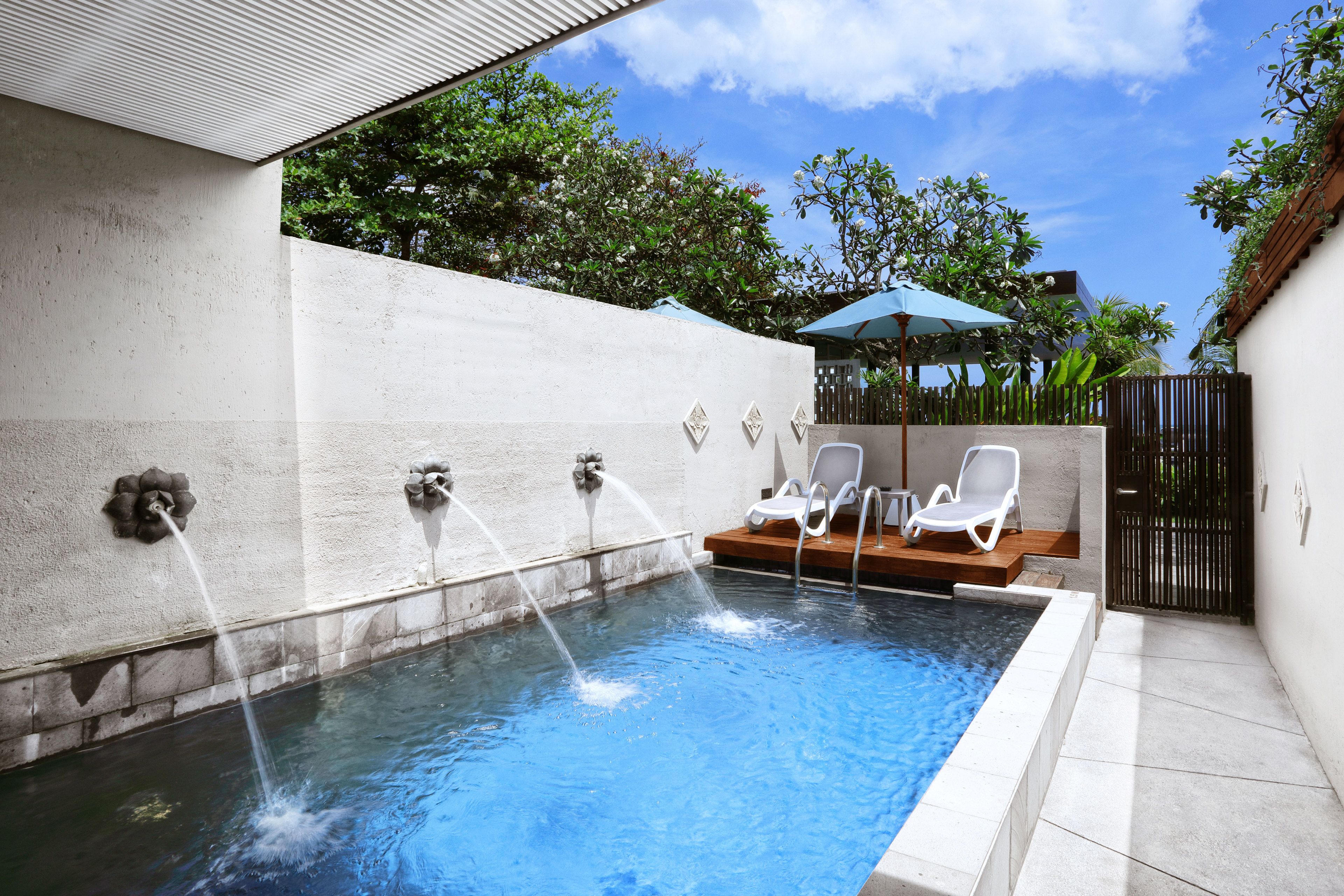 A swimming pool with water jets, a sun umbrella, and lounge chairs.