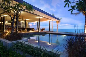 A modern outdoor pool area with a view of the ocean, surrounded by lush greenery and palm trees. - The Anvaya Beach Resort Bali (Kuta)