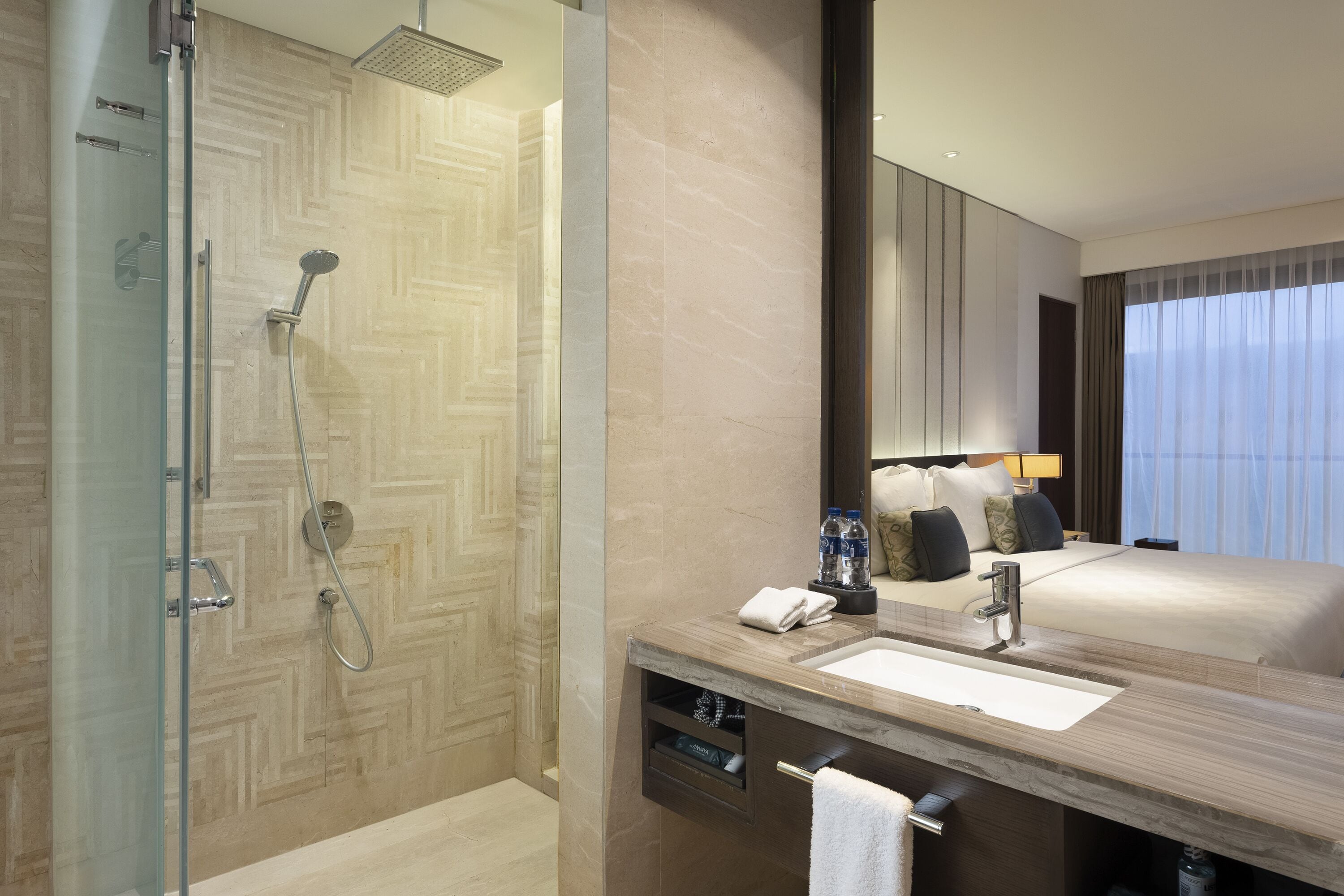 A modern hotel bathroom with a glass-enclosed shower, a wooden vanity with a sink, and a large mirror.