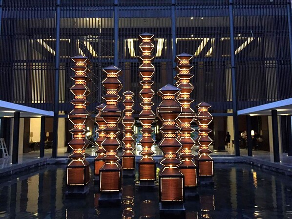 A modern building with a reflective pool and a series of illuminated lanterns in front.