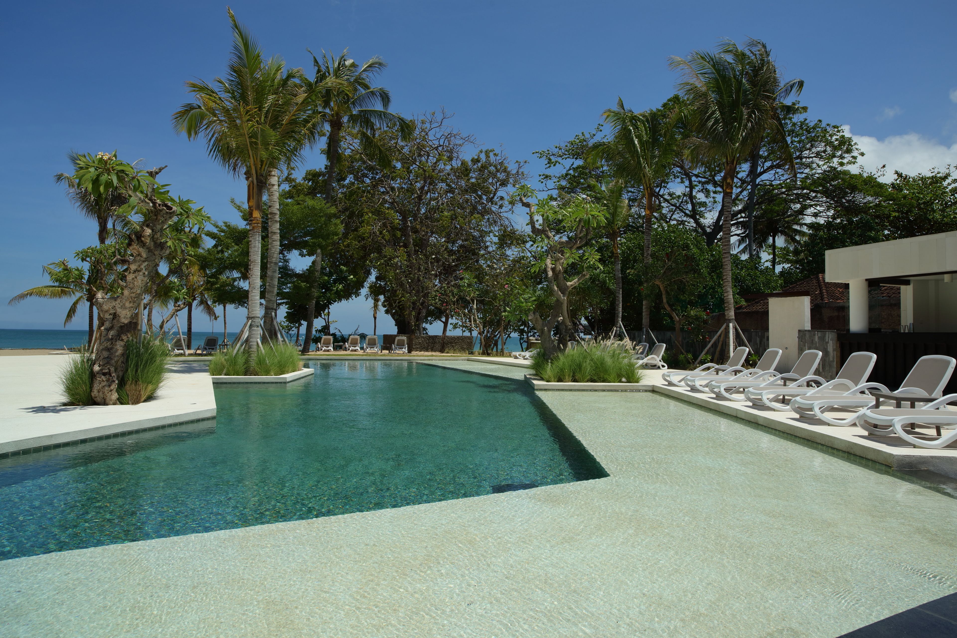 A clear pool with lounge chairs and palm trees, surrounded by a modern building.