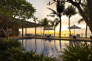 A poolside area with lounge chairs and umbrellas, overlooking the ocean at sunset.
