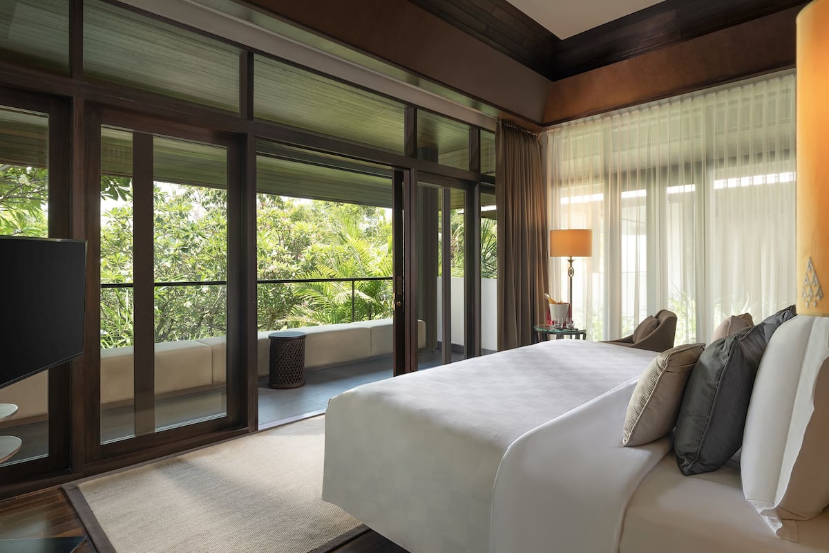 A spacious bedroom with a large bed, a TV, and a balcony with a view of greenery.